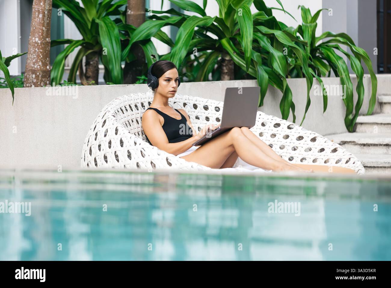 Frau mit Kopfhörern, die in einem tropischen Umfeld arbeitet oder studiert. Das Konzept von Remote-Arbeit, Flexibilität und Business in jeder Umgebung. Stockfoto