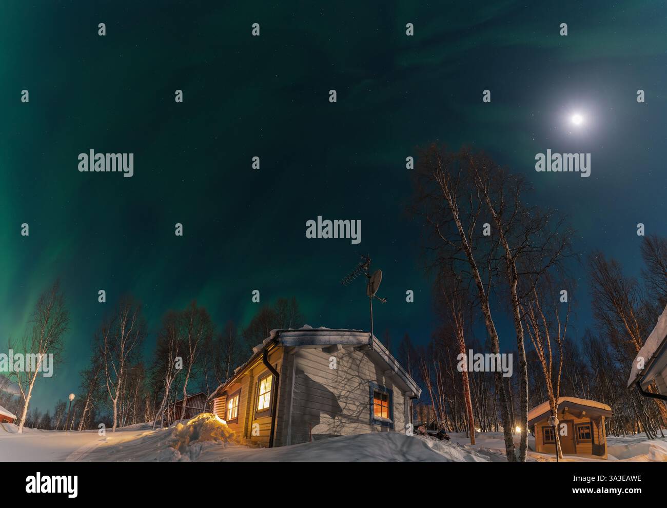 Leuchtende Nordlichter, die den Nachthimmel über einer gemütlichen Holzhütte in einer verschneiten Landschaft im schwedischen Lappland bemalen, schaffen einen magischen Winter Stockfoto