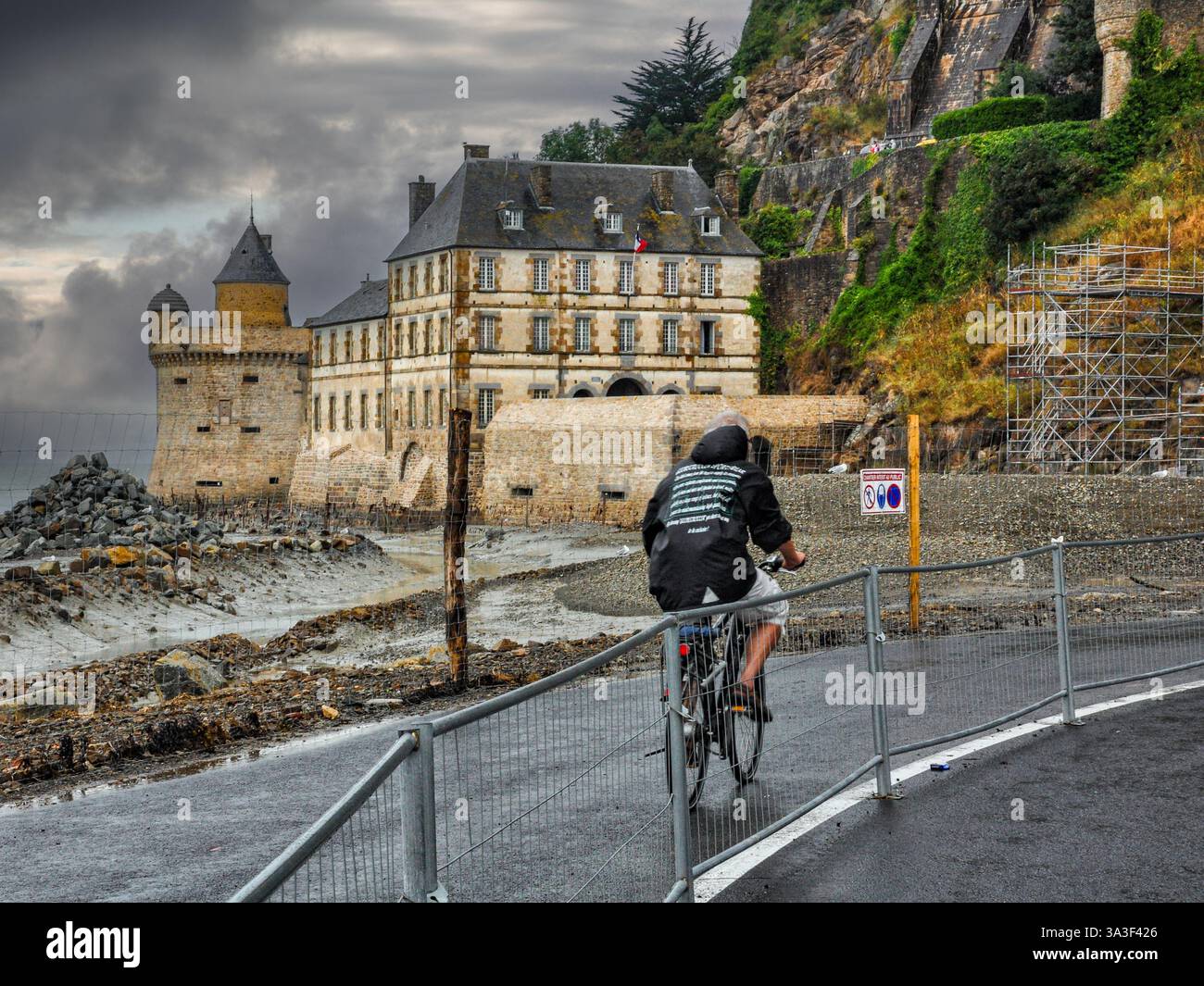 „Regnerische Ankunft: Ein Radfahrer nähert sich dem Mont Saint Michel ohne Angst vor Regen Stockfoto