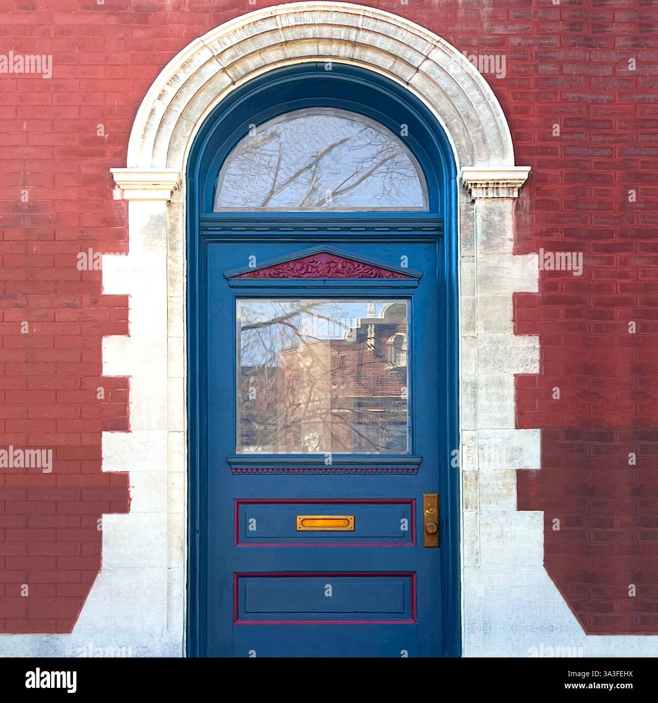 Bllue-Tür mit verziertem Rot, eingebettet in eine historische rote Backstein- und Kalksteinfassade, mit einem bogenförmigen Heckfenster und architektonischen Elementen. - Smartphone-aufgenommenes Stockfoto