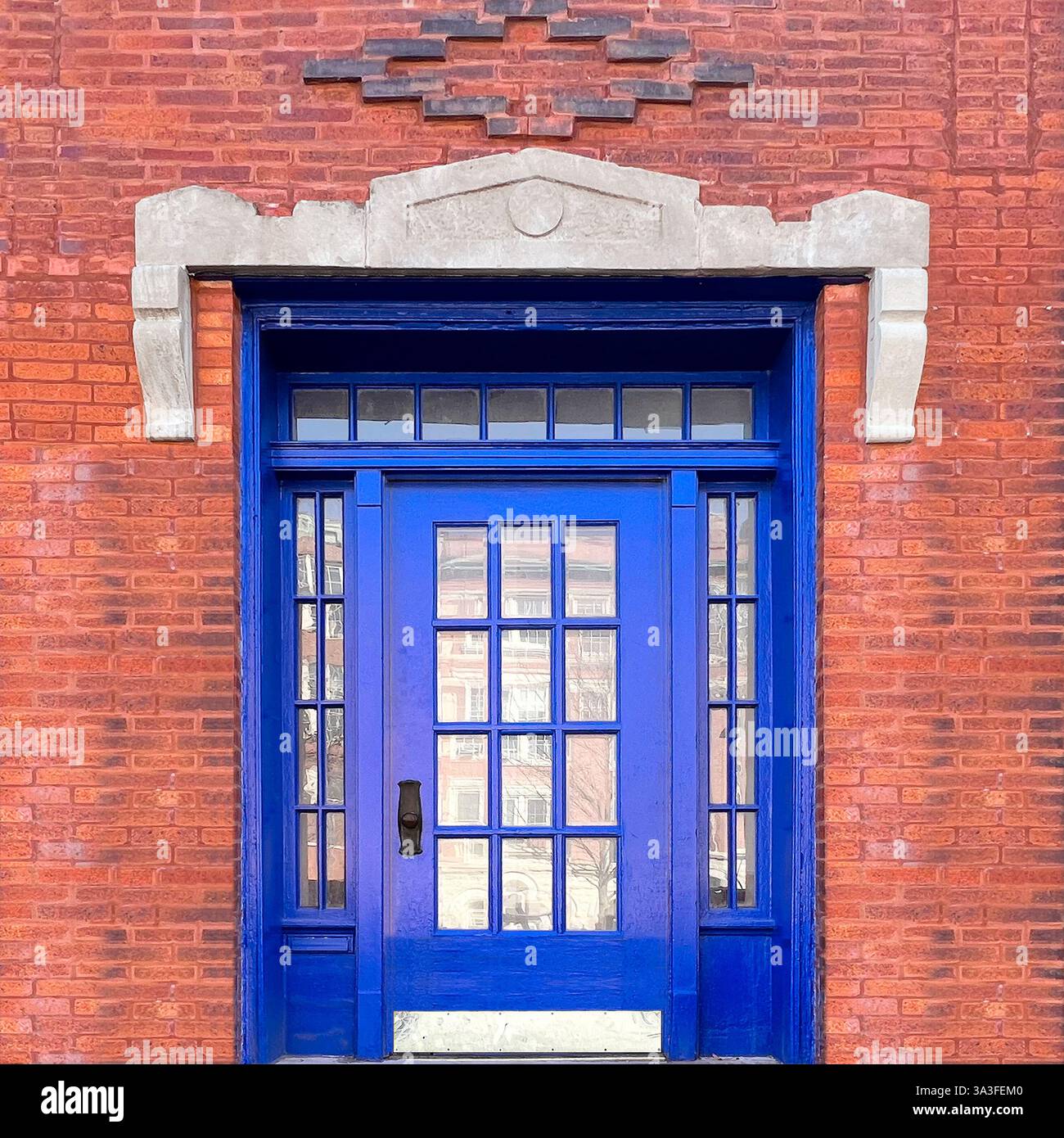 Kobaltblaue Tür mit Glasscheiben, die durch ein diamantförmiges Ziegelmuster und geometrische Steinrahmen hervorgehoben werden. - Smartphone-aufgenommenes Stockfoto