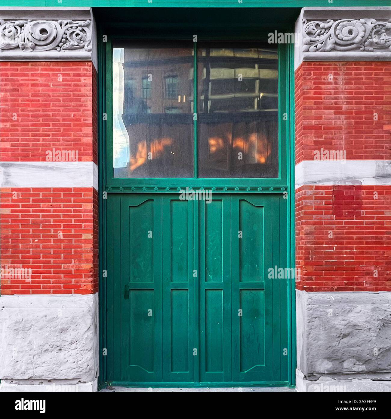 Alte grüne Tür mit großen Glaspaneelen in einer historischen roten Backsteinfassade mit filigranen Blumensteinschnitzereien. - Smartphone-aufgenommenes Stockfoto