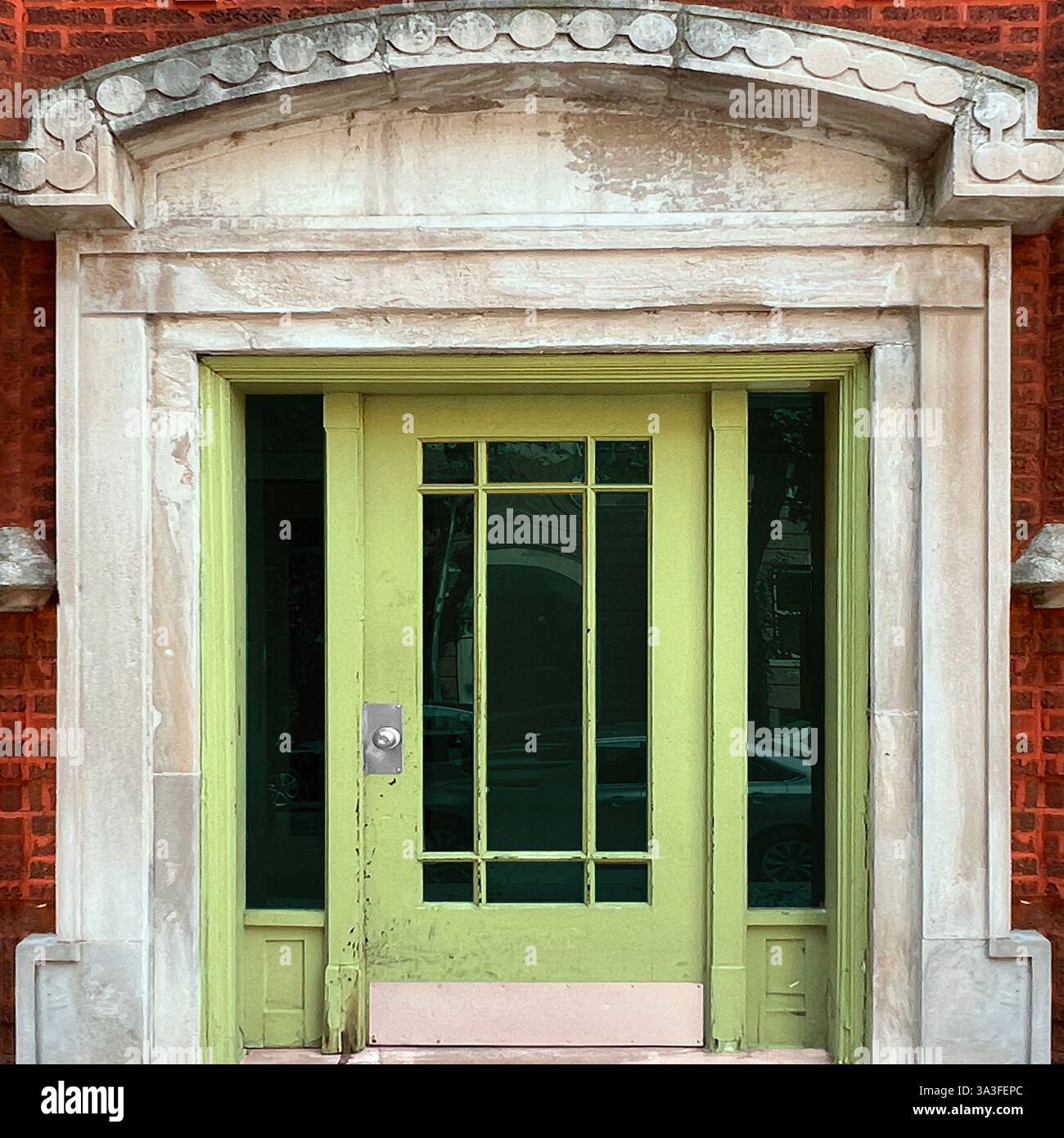 Alte, lindgrüne Glastäfelungstür in einer kunstvollen Stein- und roten Ziegelfassade mit dekorativen architektonischen Details. Stockfoto