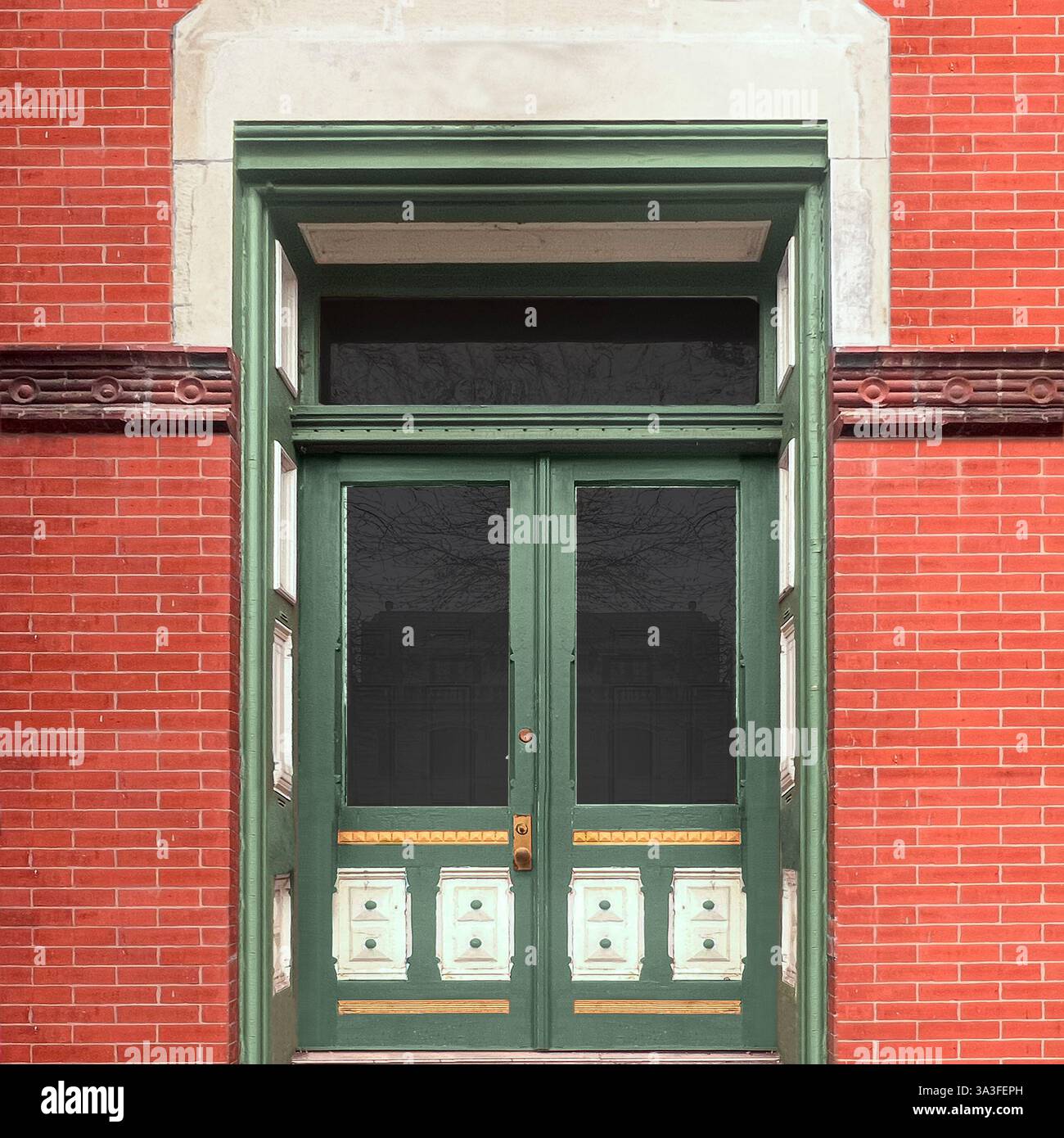 Vintage-grüne Doppeltüren mit komplizierten Paneeldetails in einer historischen roten Backsteinfassade mit dekorativen Heckfenstern. - Smartphone-aufgenommenes Stockfoto