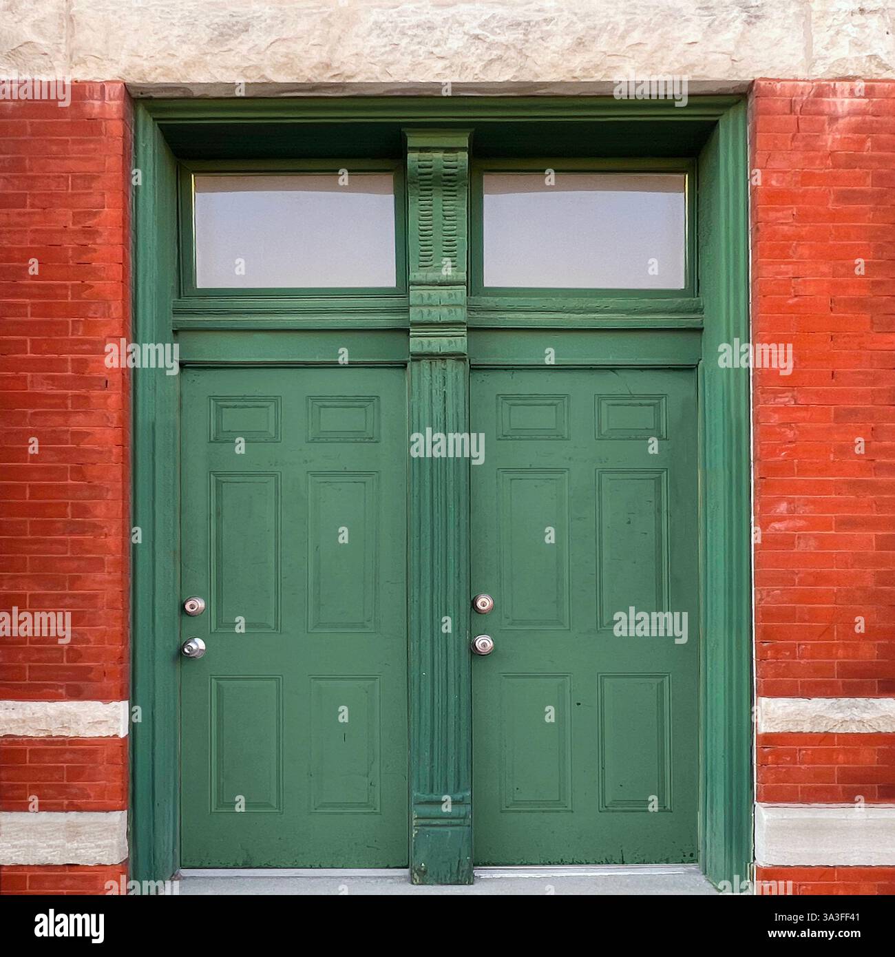 Symmetrische, grüne Doppeltüren mit komplizierten Holzarbeiten, eingerahmt von roten Ziegel- und Kalksteinakzenten, eine historische Fassade des Chicagoer Gebäudes. Stockfoto