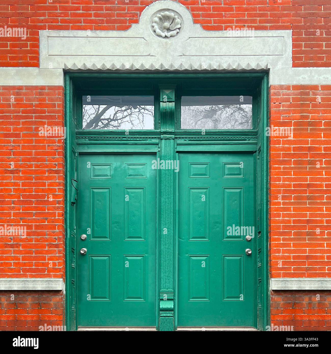 Klassische grüne Doppeltüren mit komplizierten Zierleisten und Heckfenstern, eingerahmt von einer roten Ziegelfassade mit dekorativen Steindetails. - Smartphone-aufgenommenes Stockfoto