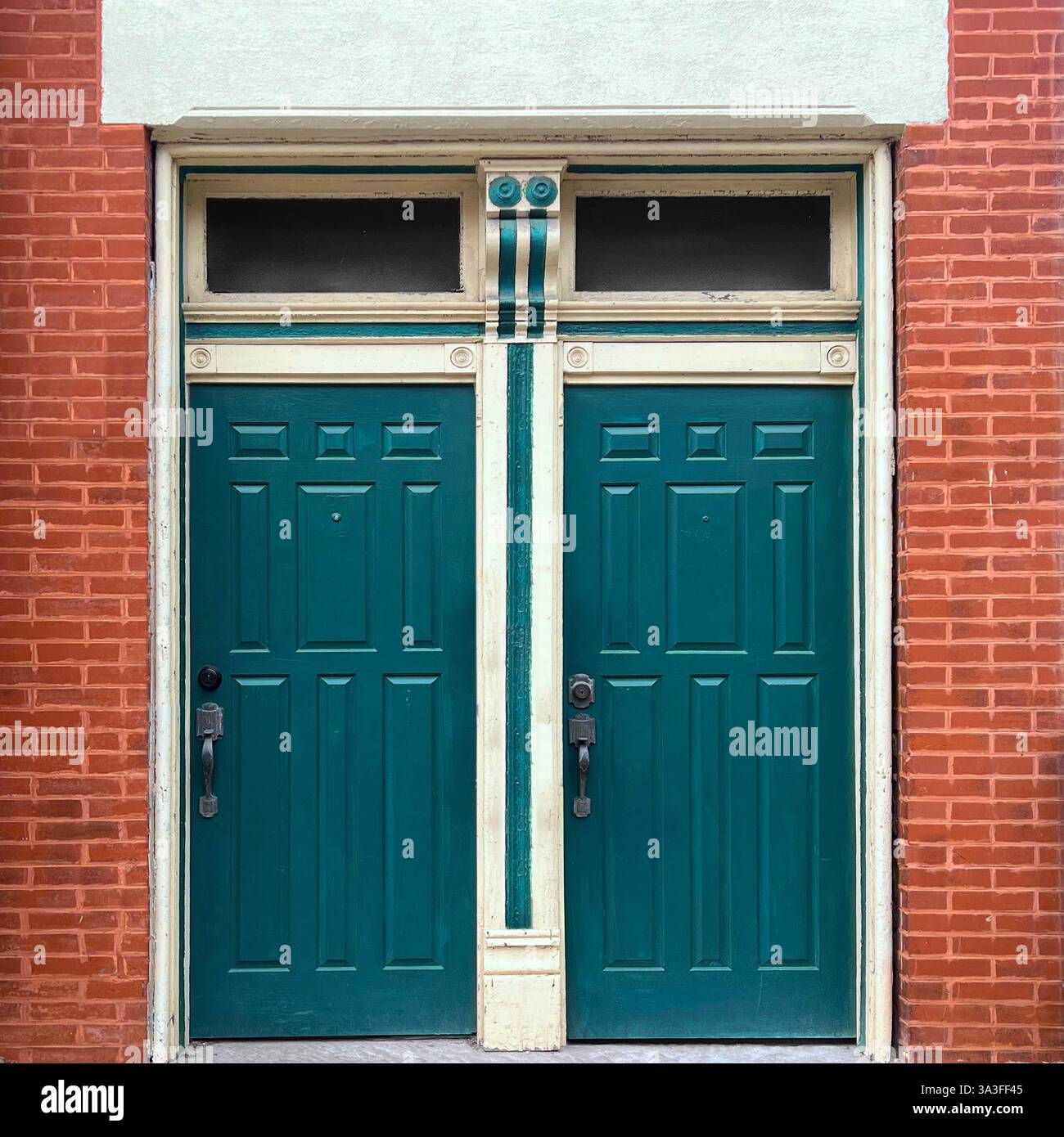 Vintage-Doppeltüren in Grün mit dekorativen Zierleisten und Heckfenstern in einer roten Ziegelfassade. - Smartphone-aufgenommenes Stockfoto