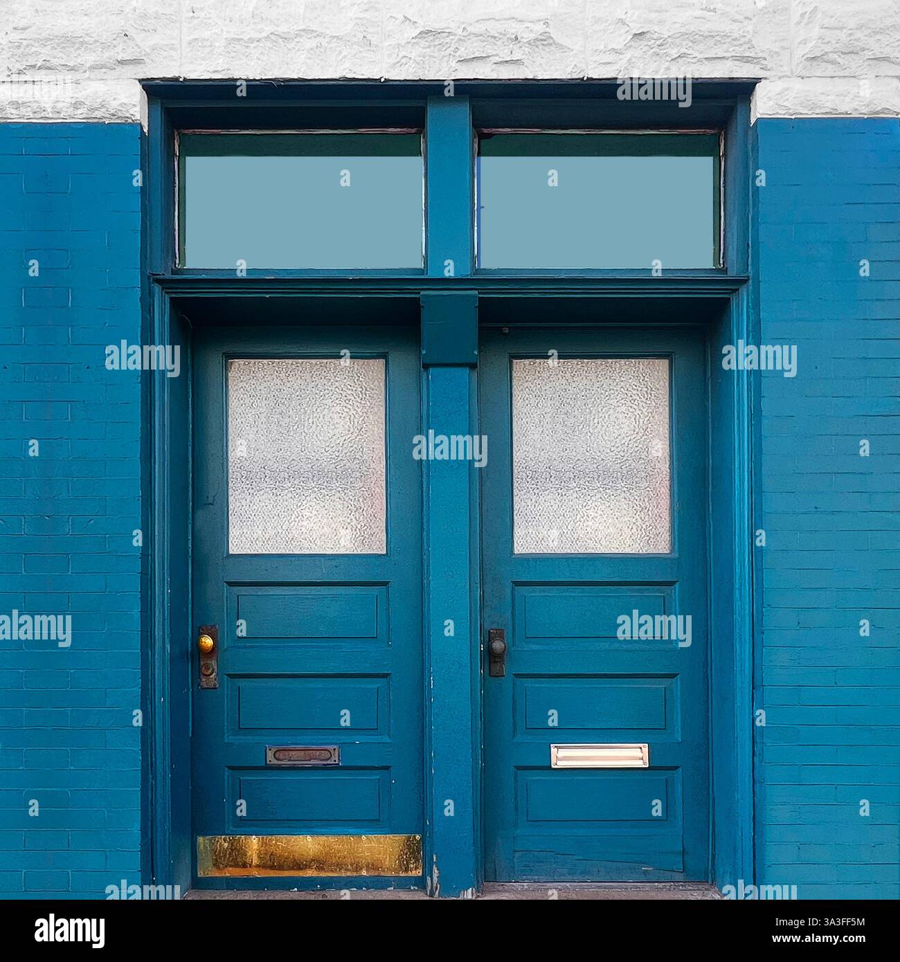 Blaue Außentüren mit strukturierten Glaspaneelen in einer blauen Ziegelfassade mit weißen Steindetails. - Smartphone-aufgenommenes Stockfoto