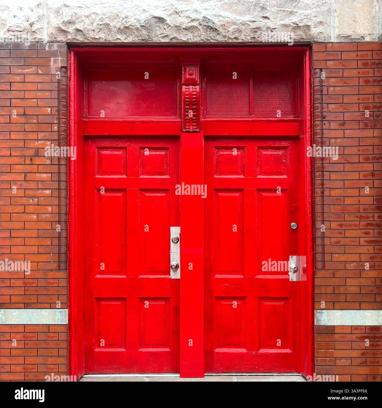 In kräftigen roten Doppeltüren, die sich in einer Ziegelstein- und Steinfassade befinden und mit klassischen architektonischen Details in einem urbanen Ambiente ausgestattet sind. Stockfoto