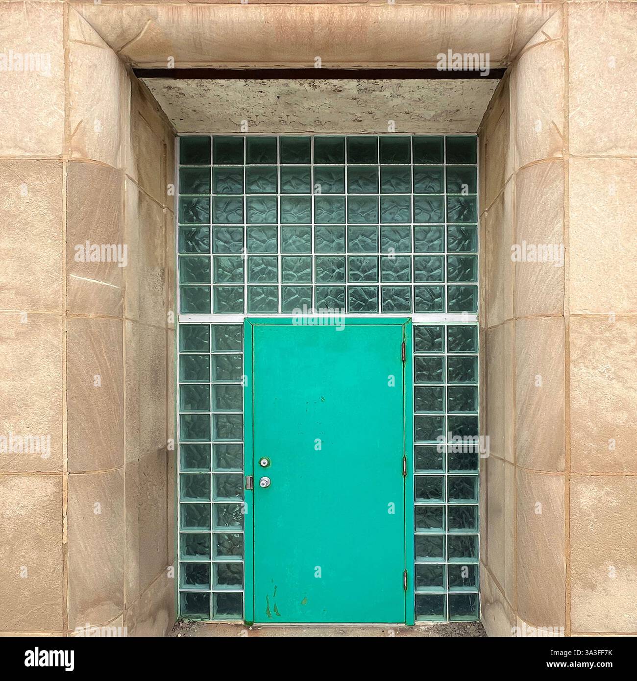 Türkisfarbene Tür, die vor einer Wand aus Glasblöcken steht und von großen Sandsteinsäulen eingerahmt wird, bietet eine einzigartige Mischung aus moderner und klassischer Architektur. - Smartphone-aufgenommenes Stockfoto