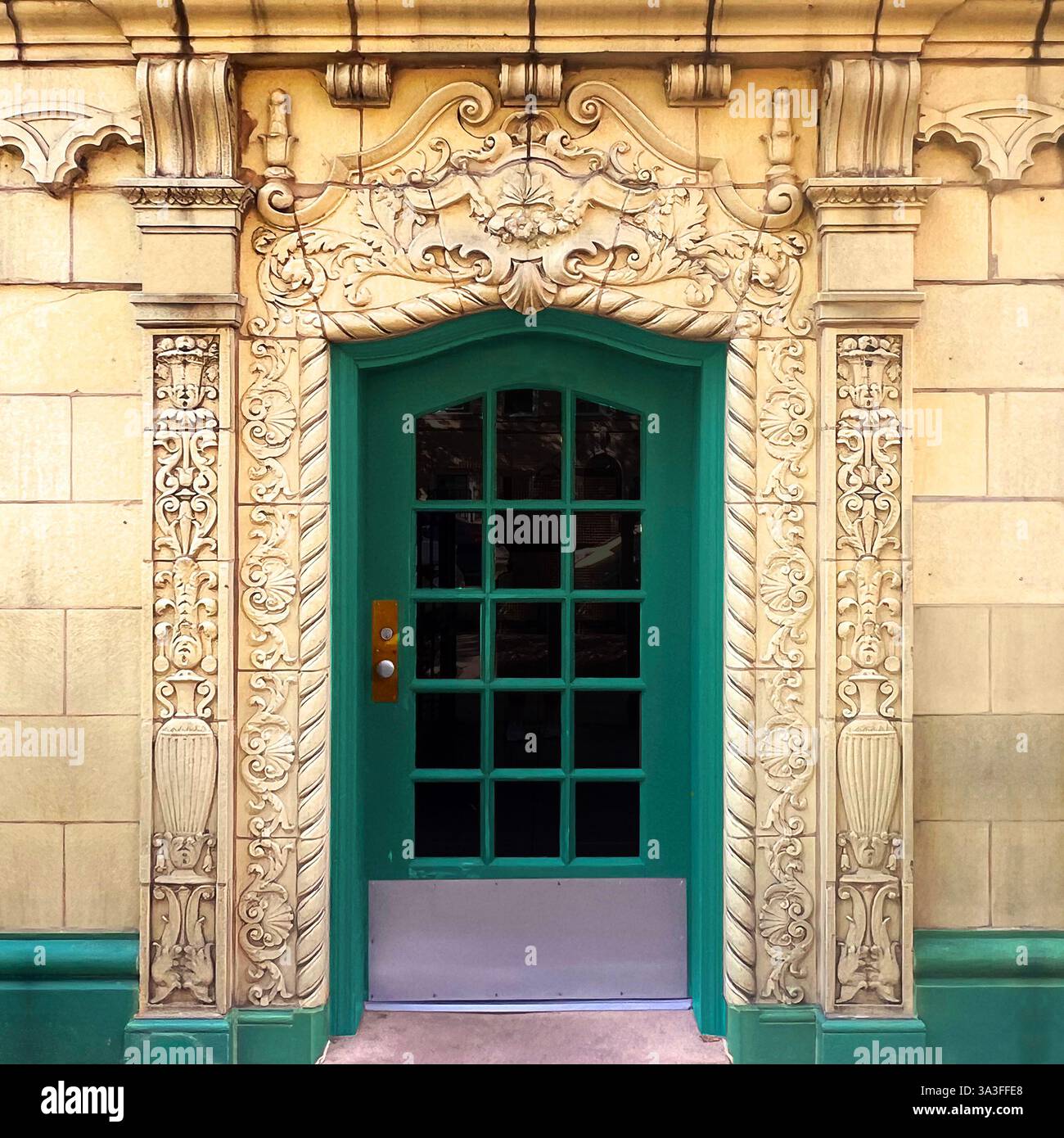 Eine historische grüne Tür mit Glasscheiben, eingerahmt von komplizierten, kunstvollen Steinschnitzereien an einer wunderschön detaillierten beigefarbenen Fassade in Chicago. Stockfoto
