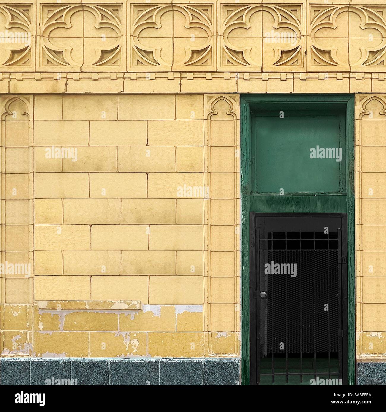Eine verwitterte grüne Tür mit einem geschlossenen Eingang in einem gelb gekachelten Gebäude mit kunstvollen geometrischen architektonischen Details in Chicago - Smartphone-aufgenommenes Stockfoto