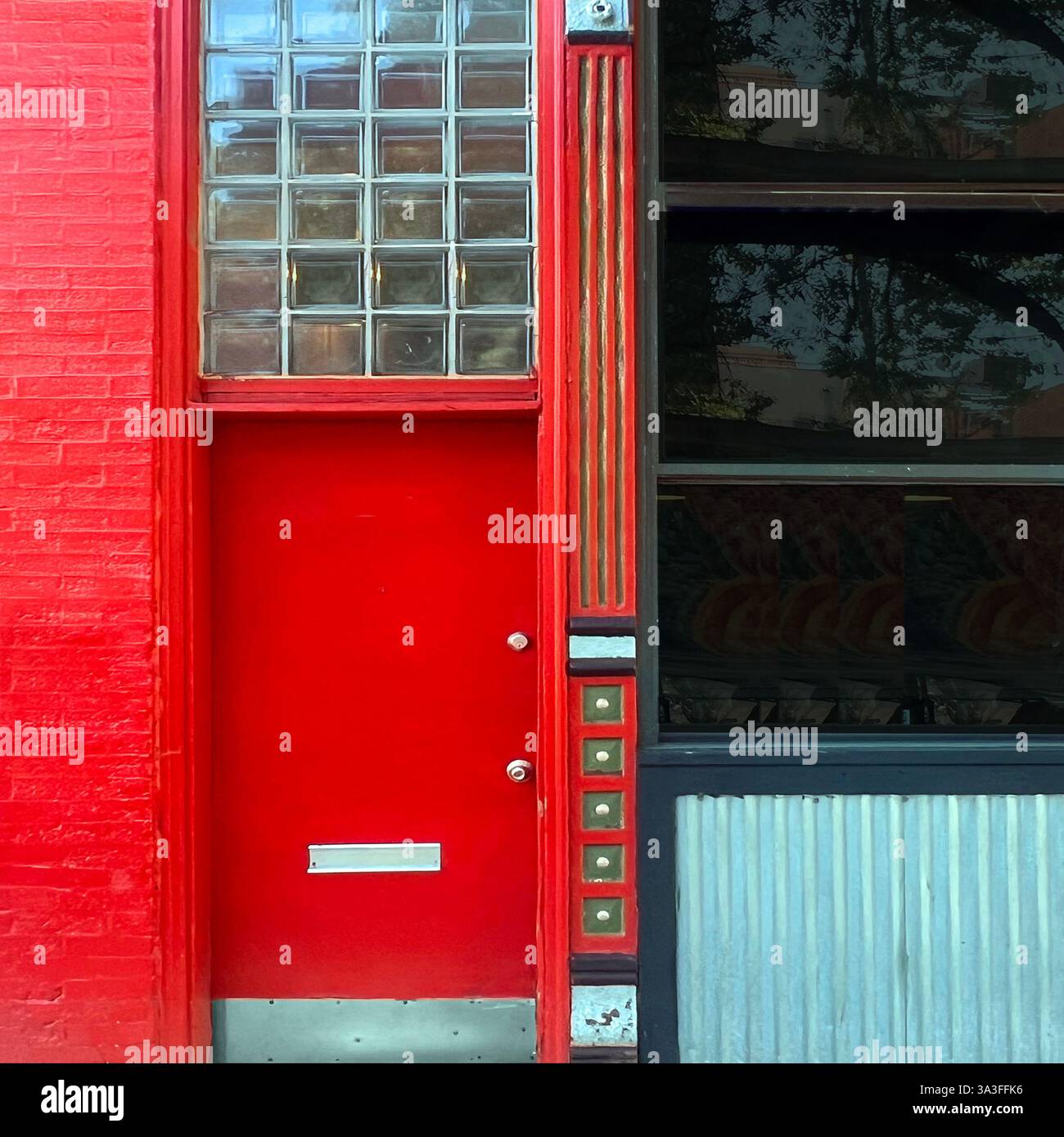 Rote Tür mit Glasblockfenstern und komplizierten Metalldetails. - Smartphone-aufgenommenes Stockfoto