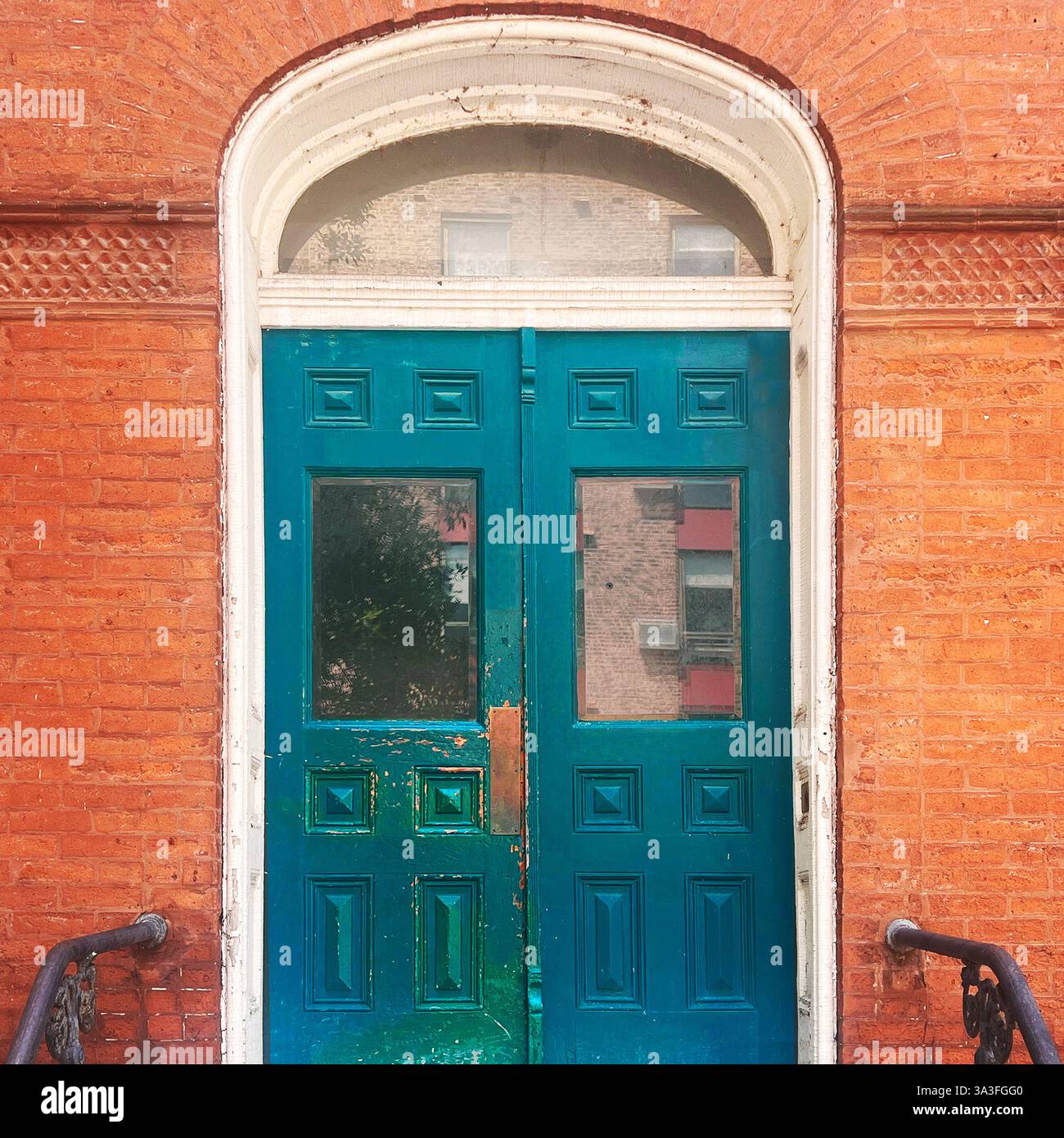 Verwitterte, türkisfarbene Doppeltüren mit Glaspaneelen und einem bogenförmigen Heckfenster in einer historischen orangen Ziegelfassade mit kunstvollen Details in Chicago. - Smartphone-aufgenommenes Stockfoto