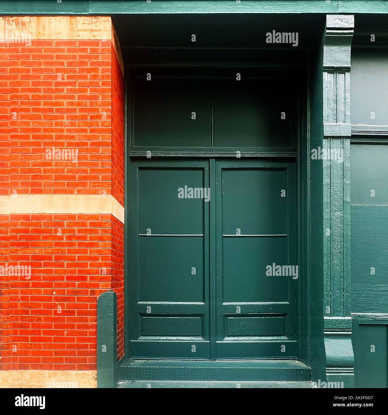 Dunkelgrüne Doppeltüren in einer reich strukturierten roten Ziegelfassade mit kontrastierenden cremefarbenen Steinakzenten in Chicago. - Smartphone-aufgenommenes Stockfoto