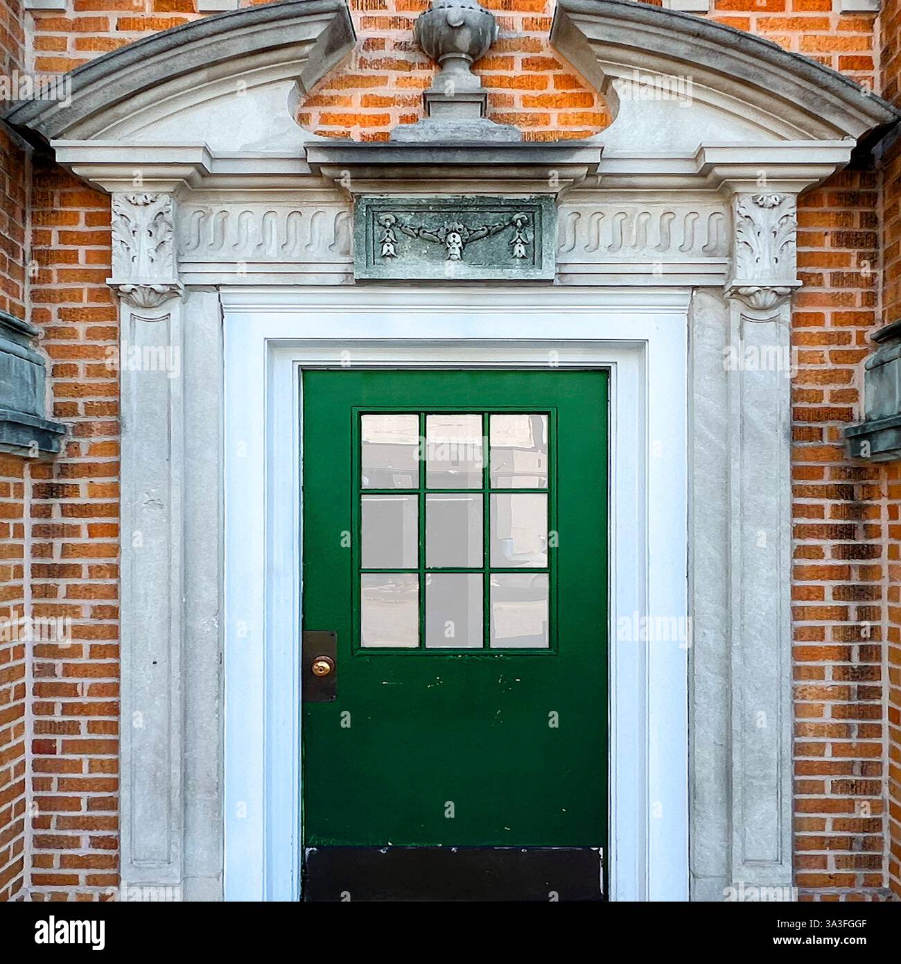 Grüne Tür mit Glasscheiben, eingerahmt von einem kunstvollen Steineingang mit dekorativen Schnitzereien und einem Giebel in einer orangen Ziegelfassade in Chicago. Stockfoto Grüne Tür mit Glasscheiben, eingerahmt von einem kunstvollen Steineingang mit dekorativen Schnitzereien und einem Giebel in einer orangen Ziegelfassade in Chicago. Stockfoto