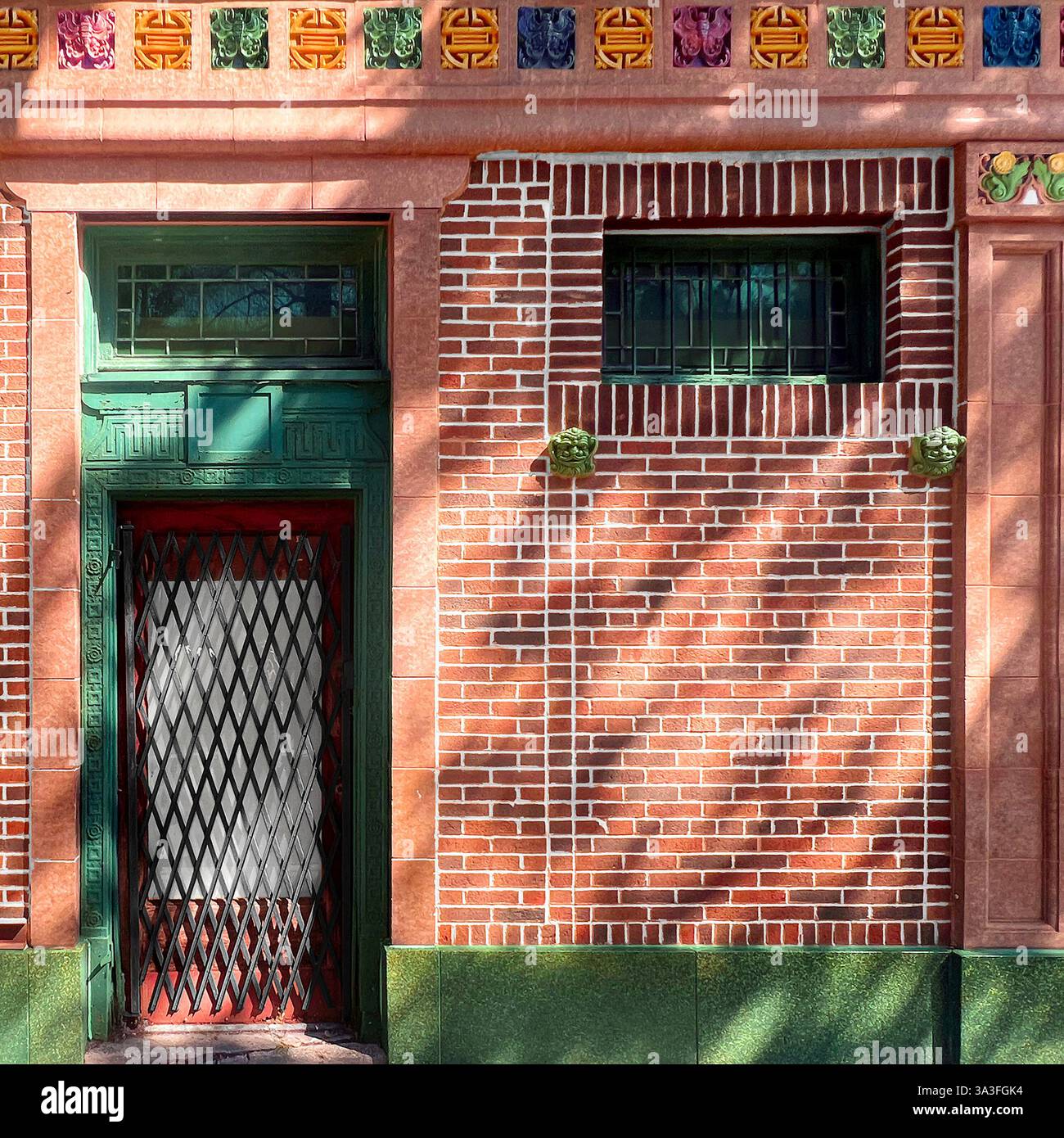 Grüne Tür, umgeben von komplexen architektonischen Details, farbenfrohen Terrakotta-Akzenten und rosafarbener Ziegelfassade in Chicagos Chinatown. - Smartphone-aufgenommenes Stockfoto