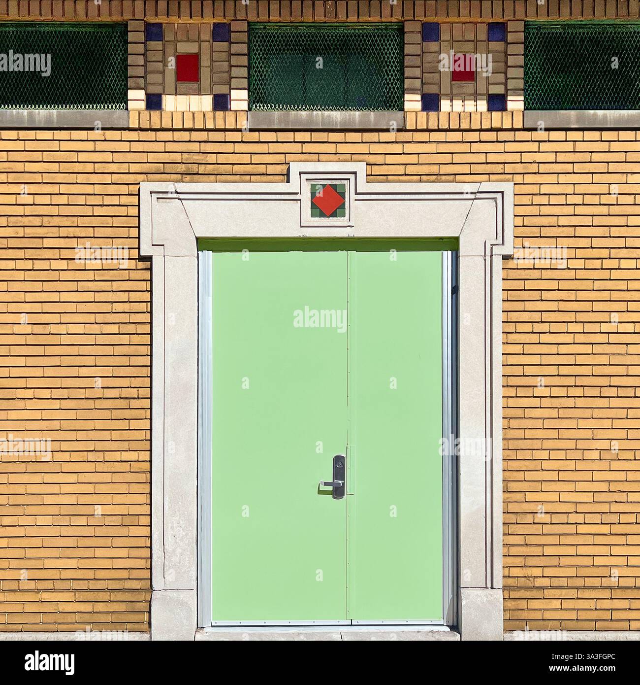 Mintgrüne Doppeltüren, eingerahmt von einem geometrischen Art déco-Steinbogen mit bunten Fliesenakzenten, in einer gelben Ziegelfassade in Chicago. - Smartphone-aufgenommenes Stockfoto