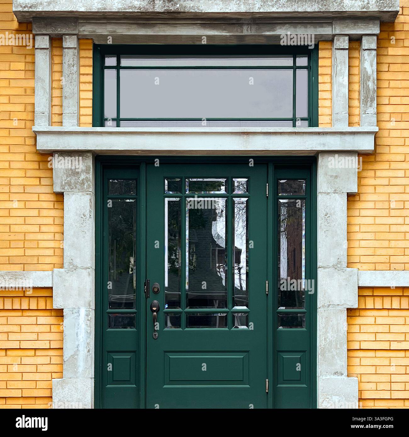 Elegante dunkelgrüne Doppeltüren mit Glaspaneelen und einem reich verzierten Heckfenster, eingerahmt von dekorativem Stein und einer gelben Ziegelfassade in Chicago. - Smartphone-aufgenommenes Stockfoto