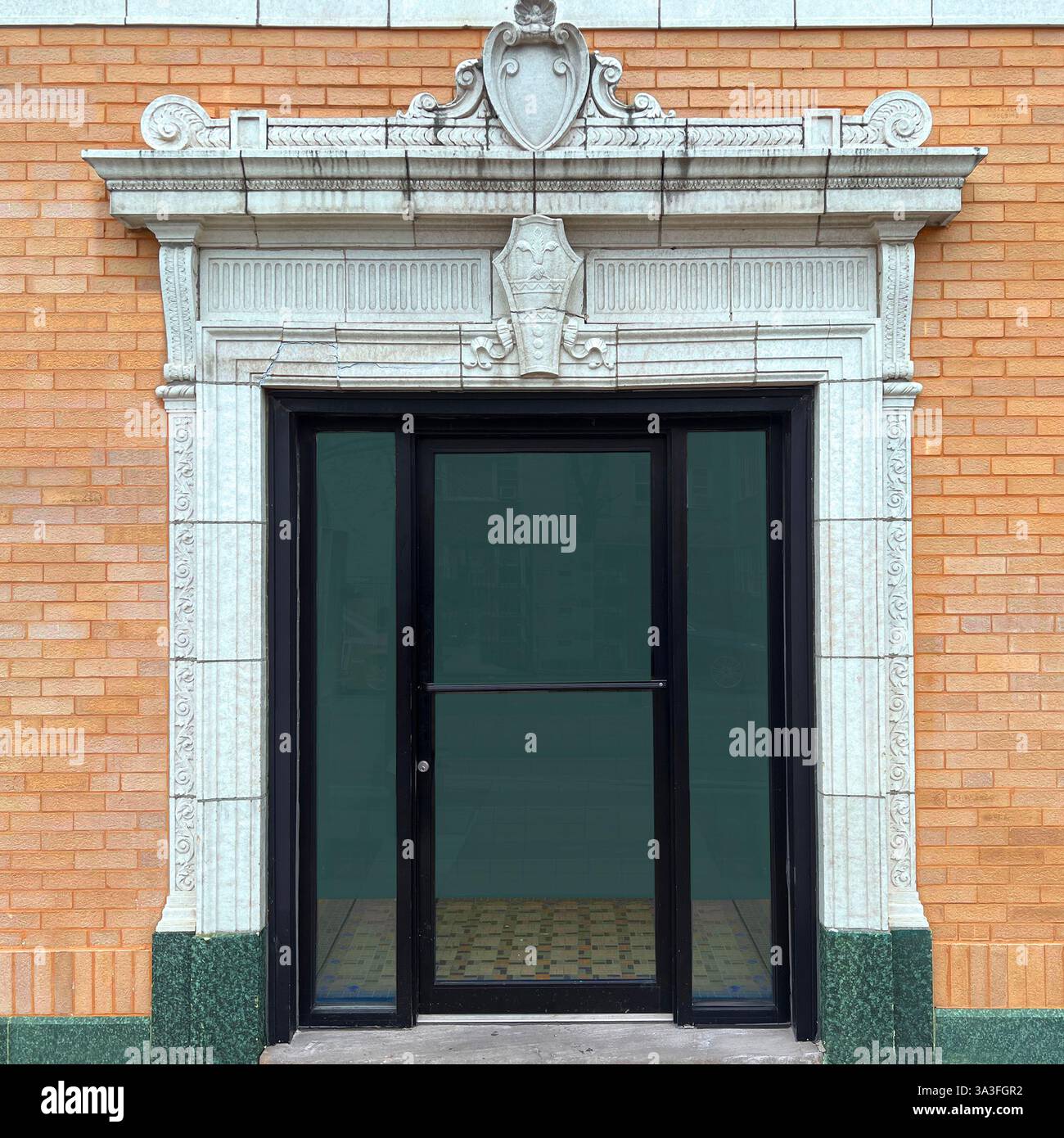 Elegante Tür in einem kunstvoll verzierten weißen Steinbogen mit komplizierten Schnitzereien, einem dekorativen Wappen und einer gelben Ziegelfassade und grünem Stein. - Smartphone-aufgenommenes Stockfoto