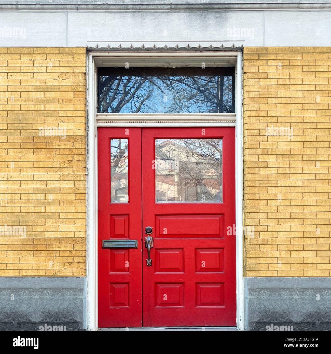 Rote Doppeltüren mit Glaspaneelen und Spiegelfenster in einer gelben Ziegelfassade mit dekorativen Zierleisten in Chicago. - Smartphone-aufgenommenes Stockfoto
