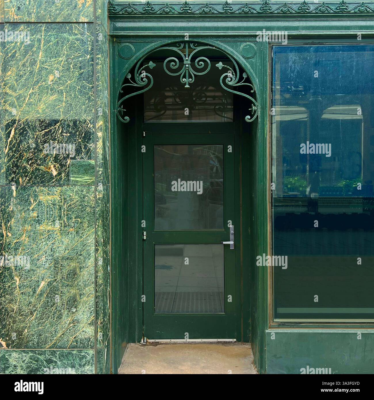 Eine dunkelgrüne Eingangstür im Jugendstilstil mit aufwändigen schmiedeeisernen Details, eingebettet in eine alte Marmor- und Glasfassade in Chicago. Stockfoto