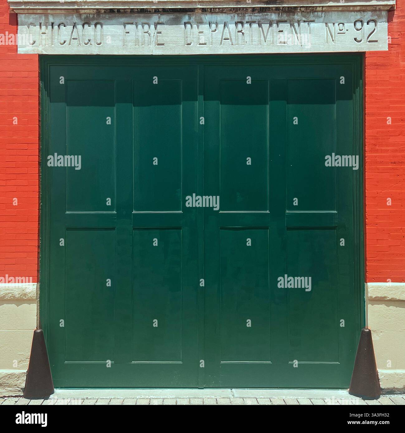 Ein grünes Tor der historischen Feuerwehr Chicago Nr. 92, eingerahmt von einer orangen Backsteinmauer, die die Architektur der städtischen Feuerwache widerspiegelt - Smartphone-aufgenommenes Stockfoto