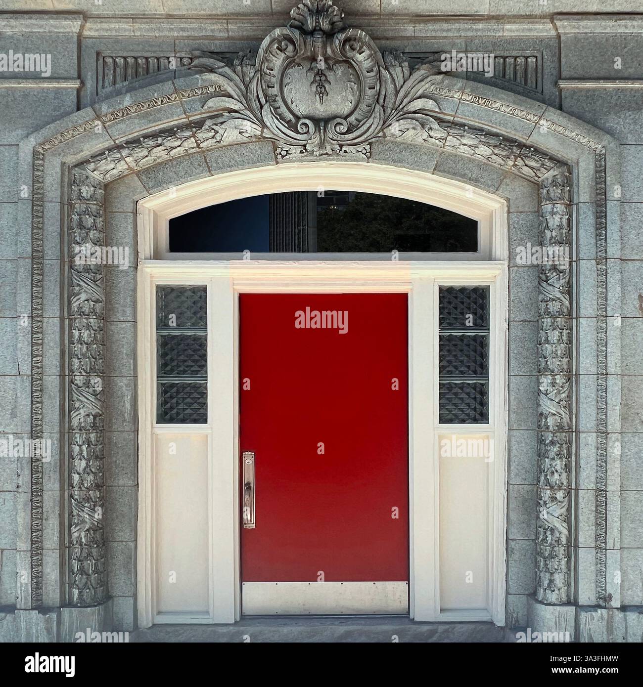 Die rote Tür wird von filigranen Steinschnitzereien und dekorativen architektonischen Details eingerahmt und schafft einen markanten Kontrast innerhalb einer historischen Gebäudefassade. Stockfoto Die rote Tür wird von filigranen Steinschnitzereien und dekorativen architektonischen Details eingerahmt und schafft einen markanten Kontrast innerhalb einer historischen Gebäudefassade. Stockfoto