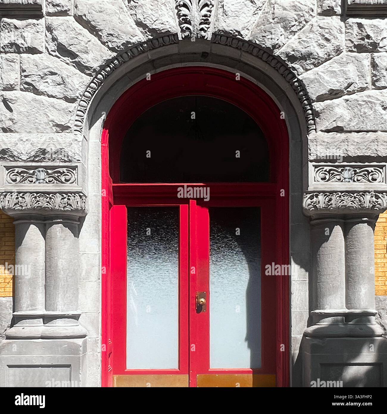 Rote Doppeltüren mit mattierten Glaspaneelen, die in einem kunstvollen Steinbogen mit komplizierten Schnitzereien und einer strukturierten historischen Fassade untergebracht sind. Stockfoto Rote Doppeltüren mit mattierten Glaspaneelen, die in einem kunstvollen Steinbogen mit komplizierten Schnitzereien und einer strukturierten historischen Fassade untergebracht sind. Stockfoto