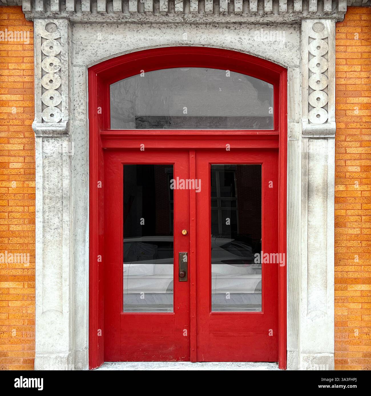 Rote Doppeltür mit bogenförmigem Heckfenster, eingerahmt von einer kunstvollen Kalksteinfassade mit komplizierten Schnitzereien, die vor einem historischen Backsteingebäude steht. Stockfoto Rote Doppeltür mit bogenförmigem Heckfenster, eingerahmt von einer kunstvollen Kalksteinfassade mit komplizierten Schnitzereien, die vor einem historischen Backsteingebäude steht. Stockfoto