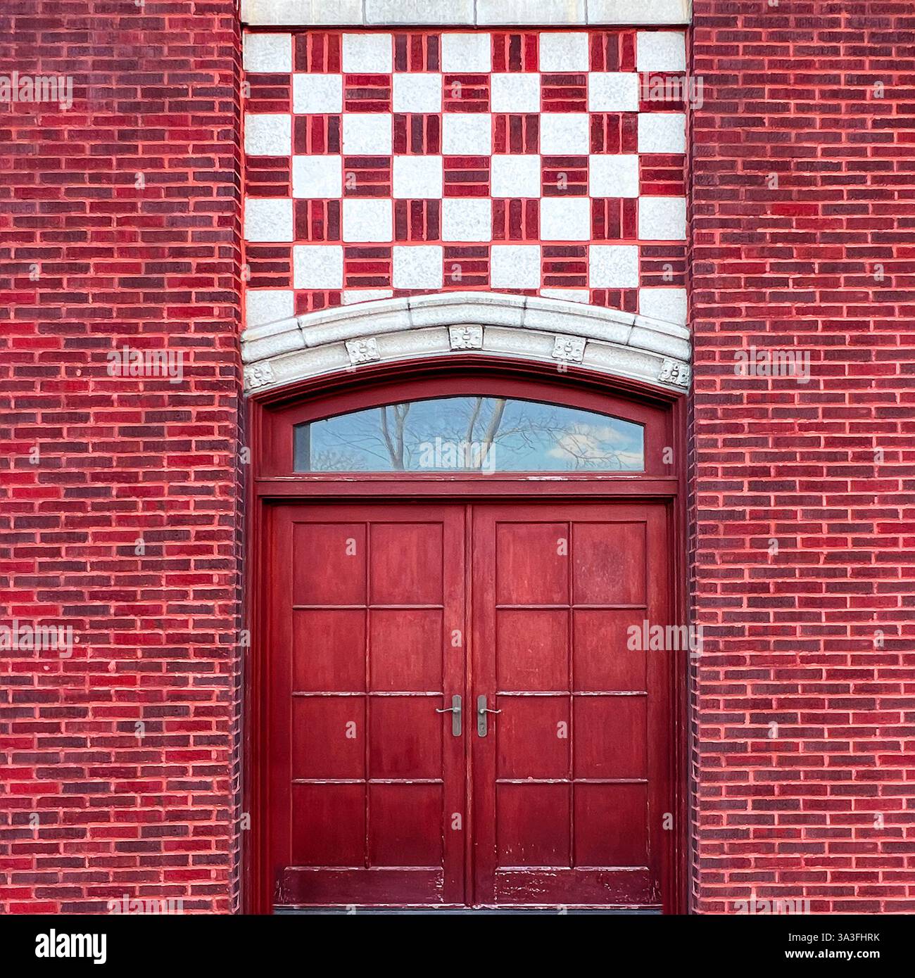 Ein historischer Eingang aus rotem Backstein mit doppelten Holztüren und einem kunstvollen Schachbrettstein in Chicago - Smartphone-aufgenommenes Stockfoto