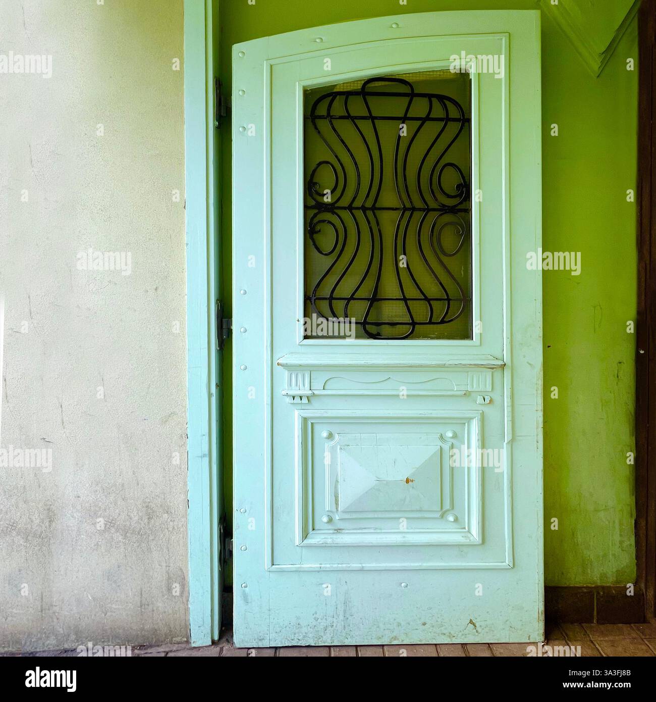 In einem historischen Gebäude in Łódź, Polen, steht eine elegante, hellgrüne Vintage-Tür mit aufwändigen Schmiedearbeiten und klassischen Paneeldetails leicht offen Stockfoto In einem historischen Gebäude in Łódź, Polen, steht eine elegante, hellgrüne Vintage-Tür mit aufwändigen Schmiedearbeiten und klassischen Paneeldetails leicht offen Stockfoto