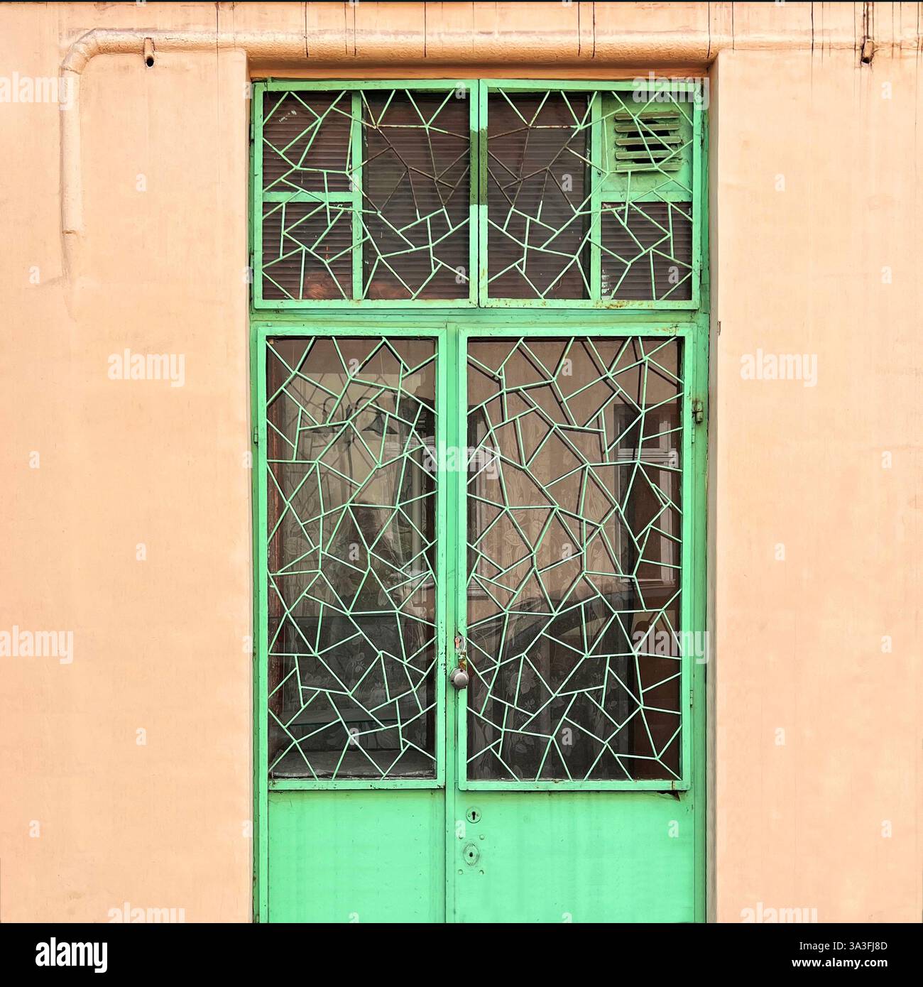 Eine einzigartige grüne Metalltür mit abstraktem geometrischem Gittermuster, die sich vor einer warmen beigefarbenen Fassade in Łódź, Polen, befindet Stockfoto