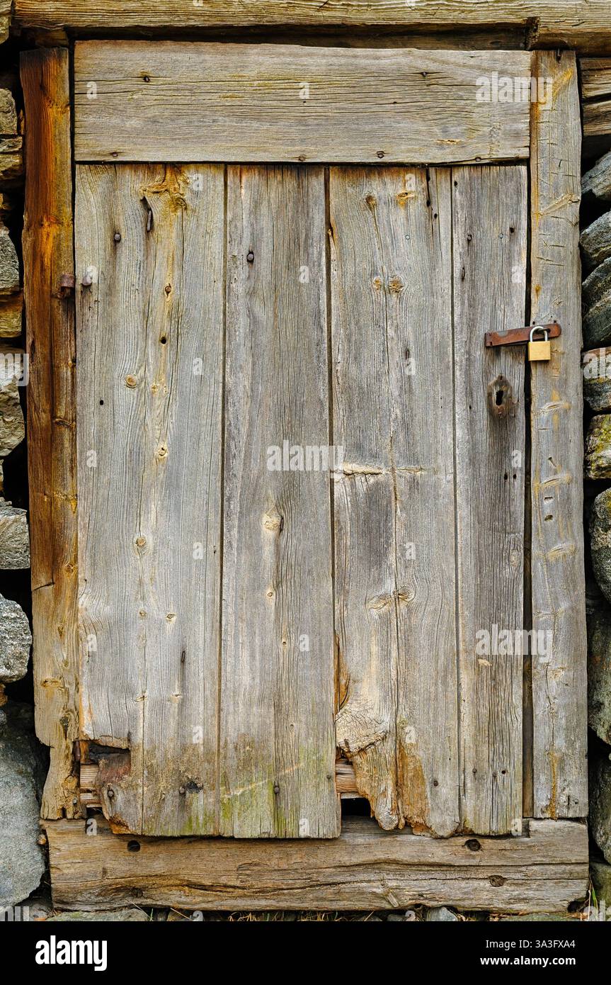 Eine verwitterte Holztür steht fest an einer Steinmauer und zeigt ihren rustikalen Charme und ihre natürliche Abnutzung. Ein Vorhängeschloss sichert sie. Stockfoto