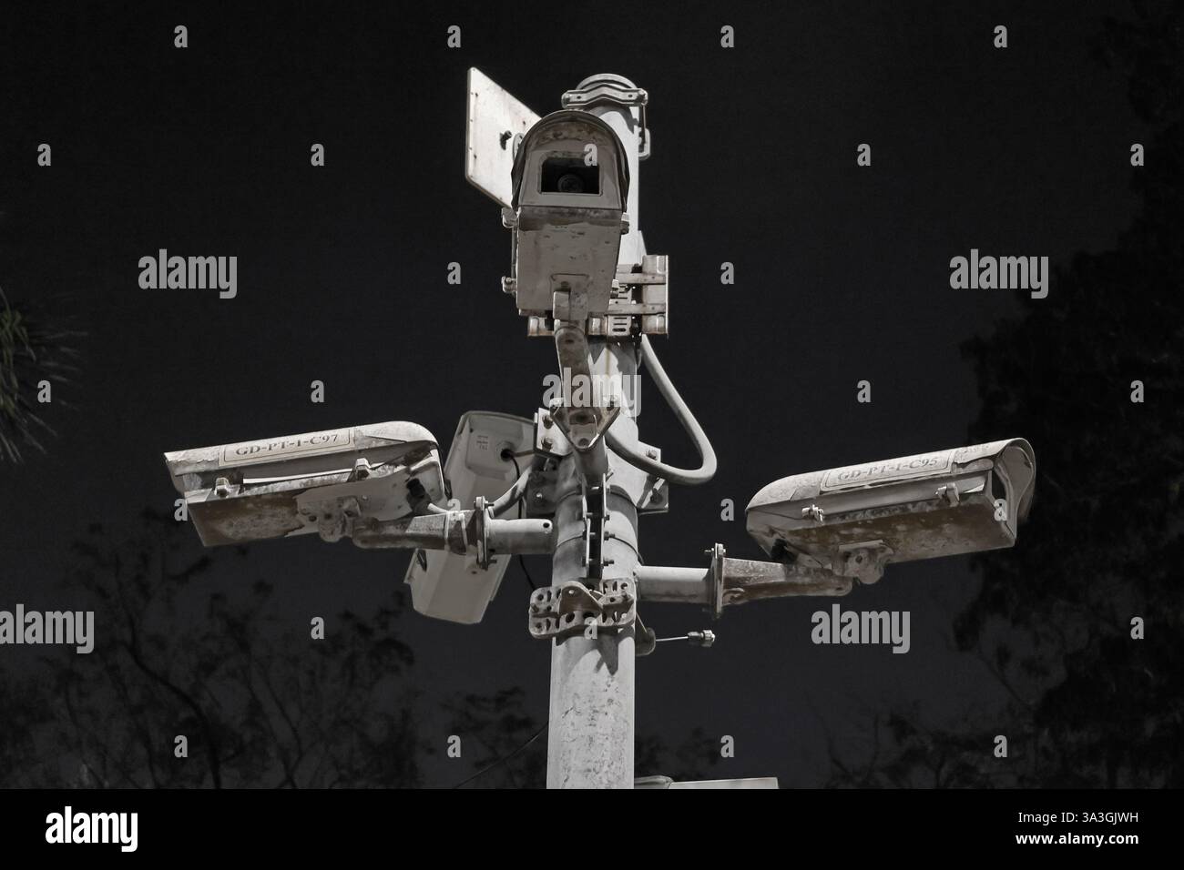 Niedrigwinkelaufnahme mehrerer alter Überwachungskameras auf einem Metallmast vor einem dunklen Himmel. Die Kameras sind verwittert und erzeugen ein dramatisches, dystopisches Gefühl. Stockfoto