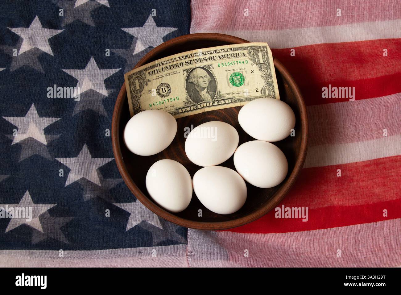 Hühnereier liegen auf einem Teller mit einem Dollar auf einer amerikanischen Flagge auf einem Küchentisch, Eiermangel in Amerika Stockfoto