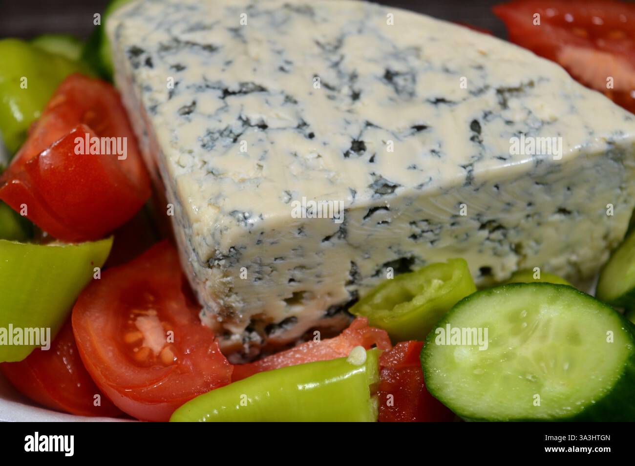 Blauschimmelkäse mit Scheiben grüner Chili, Tomaten und Gurken, Käse mit essbaren Schimmelformen, die durch den C blaugrüne Flecken oder Adern bilden Stockfoto