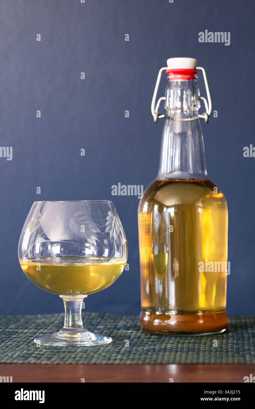 Eine klare Flasche mit Schwenkdeckel und ein Glas mit Scharfschütze auf einem Tisch vor dunkelblauem Hintergrund Stockfoto