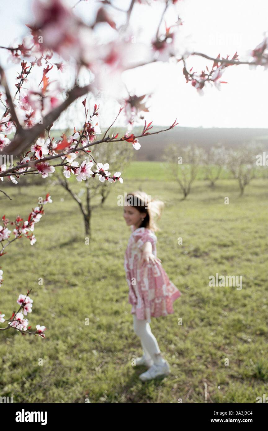 Ein fröhliches Mädchen spielt zwischen blühenden Mandelbäumen, ihr Lachen erfüllt die Frühlingsluft. Stockfoto
