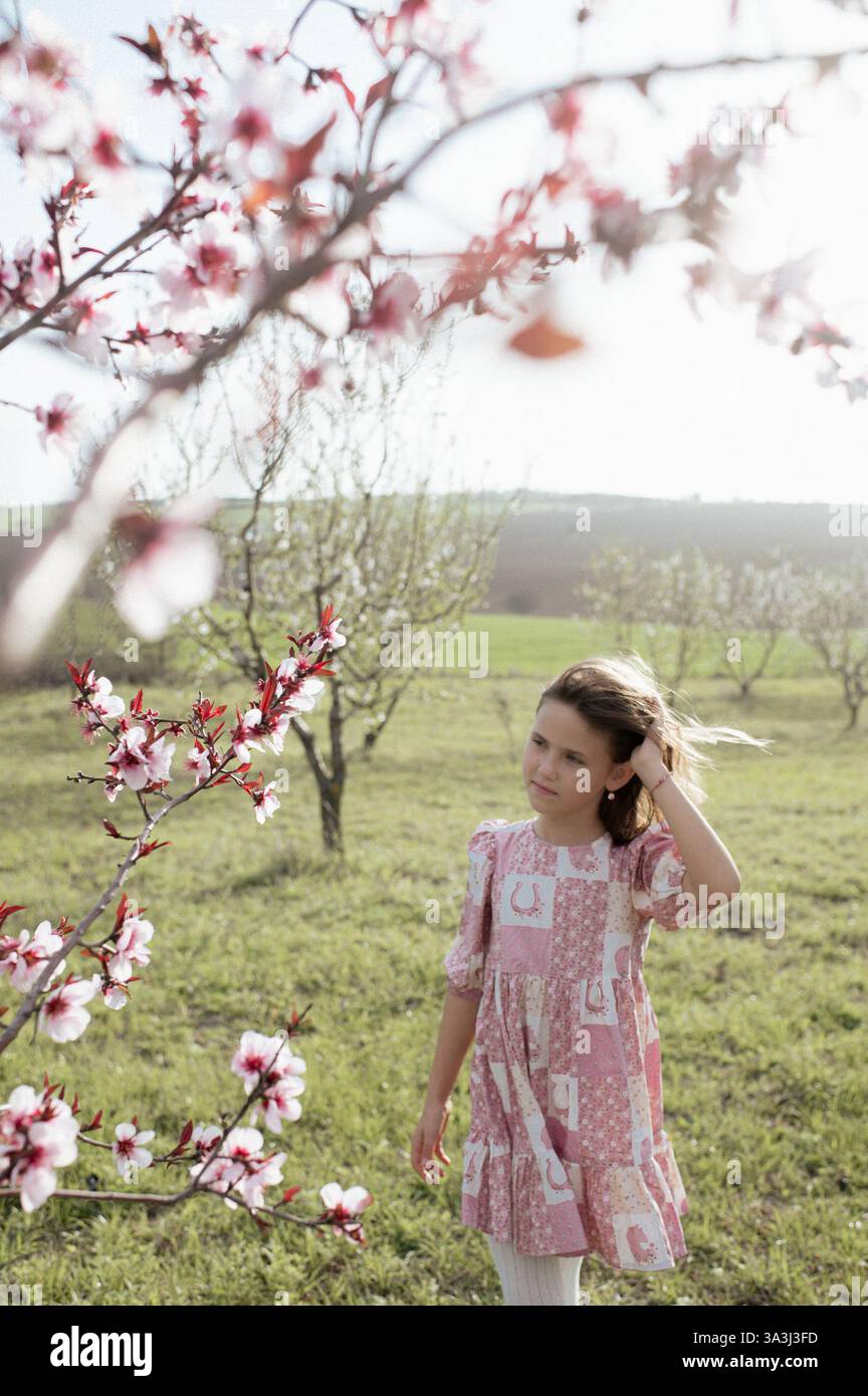 Ein fröhliches Mädchen spielt zwischen blühenden Mandelbäumen, ihr Lachen erfüllt die Frühlingsluft. Stockfoto