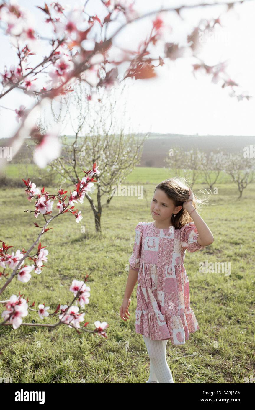 Ein fröhliches Mädchen spielt zwischen blühenden Mandelbäumen, ihr Lachen erfüllt die Frühlingsluft. Stockfoto