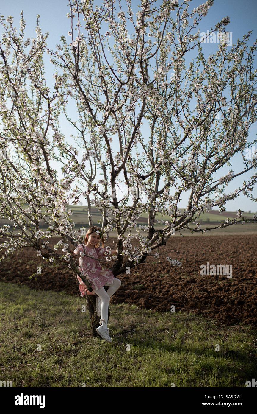 Ein fröhliches Mädchen spielt zwischen blühenden Mandelbäumen, ihr Lachen erfüllt die Frühlingsluft. Stockfoto