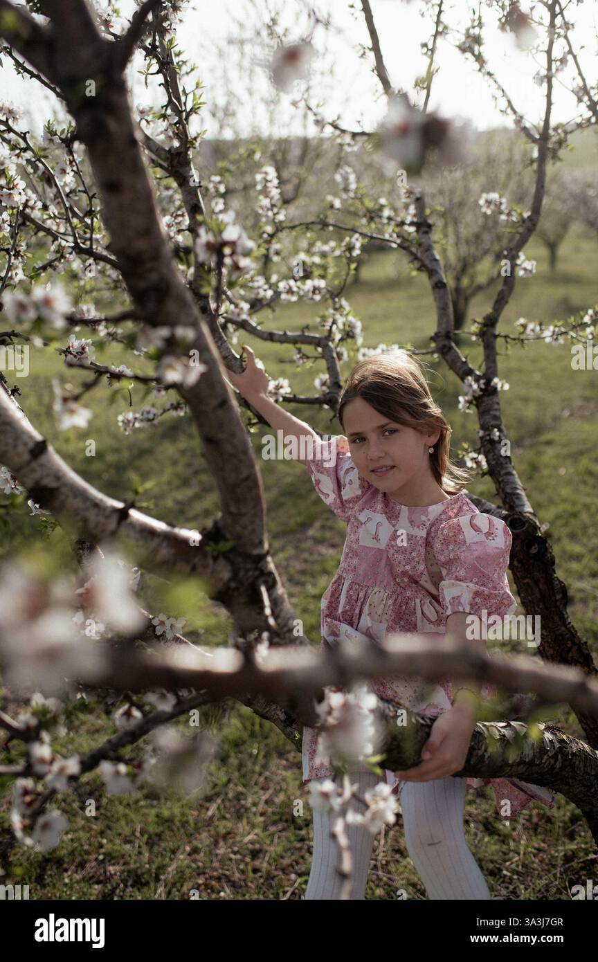 Ein fröhliches Mädchen spielt zwischen blühenden Mandelbäumen, ihr Lachen erfüllt die Frühlingsluft. Stockfoto