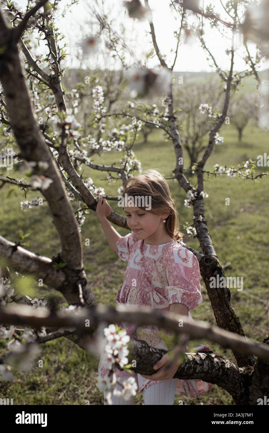 Ein fröhliches Mädchen spielt zwischen blühenden Mandelbäumen, ihr Lachen erfüllt die Frühlingsluft. Stockfoto