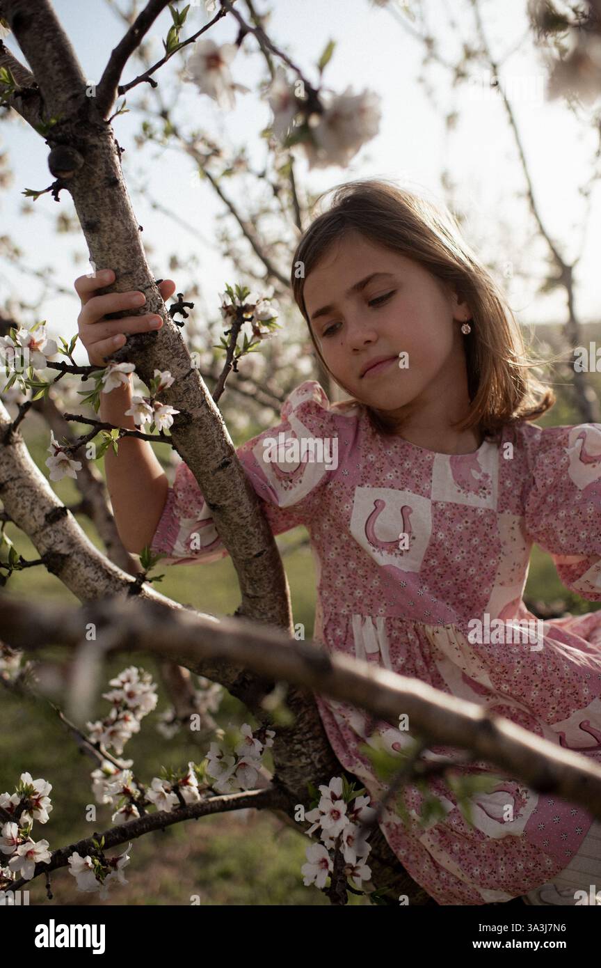 Ein fröhliches Mädchen spielt zwischen blühenden Mandelbäumen, ihr Lachen erfüllt die Frühlingsluft. Stockfoto