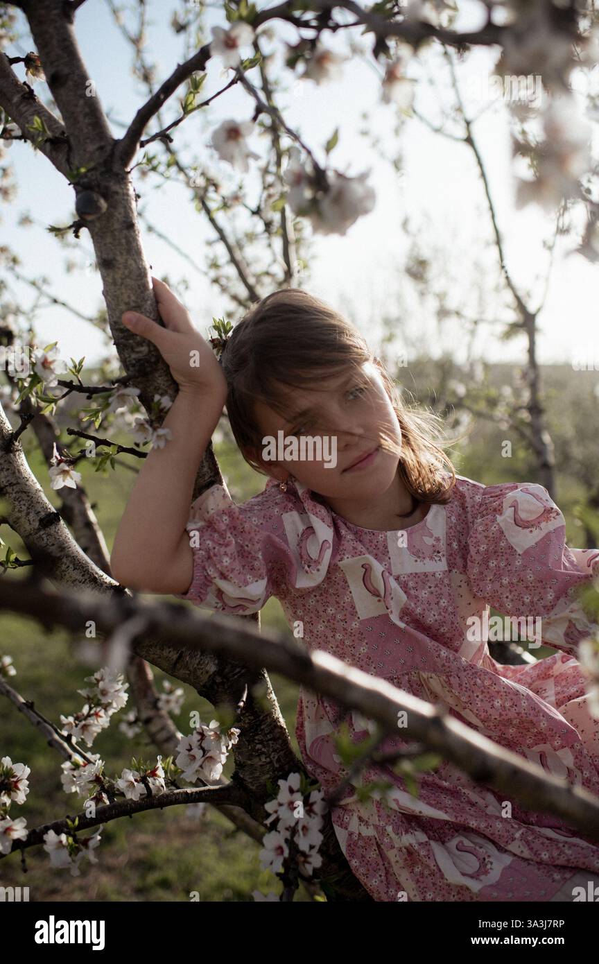 Ein fröhliches Mädchen spielt zwischen blühenden Mandelbäumen, ihr Lachen erfüllt die Frühlingsluft. Stockfoto