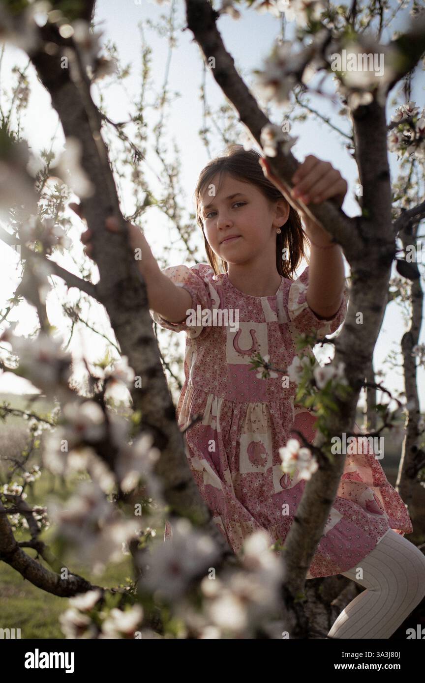 Ein fröhliches Mädchen spielt zwischen blühenden Mandelbäumen, ihr Lachen erfüllt die Frühlingsluft. Stockfoto