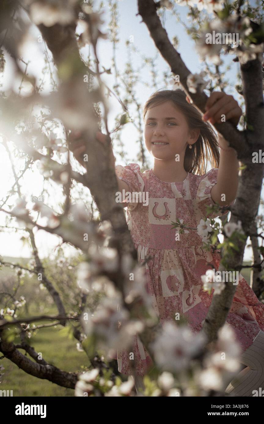 Ein fröhliches Mädchen spielt zwischen blühenden Mandelbäumen, ihr Lachen erfüllt die Frühlingsluft. Stockfoto