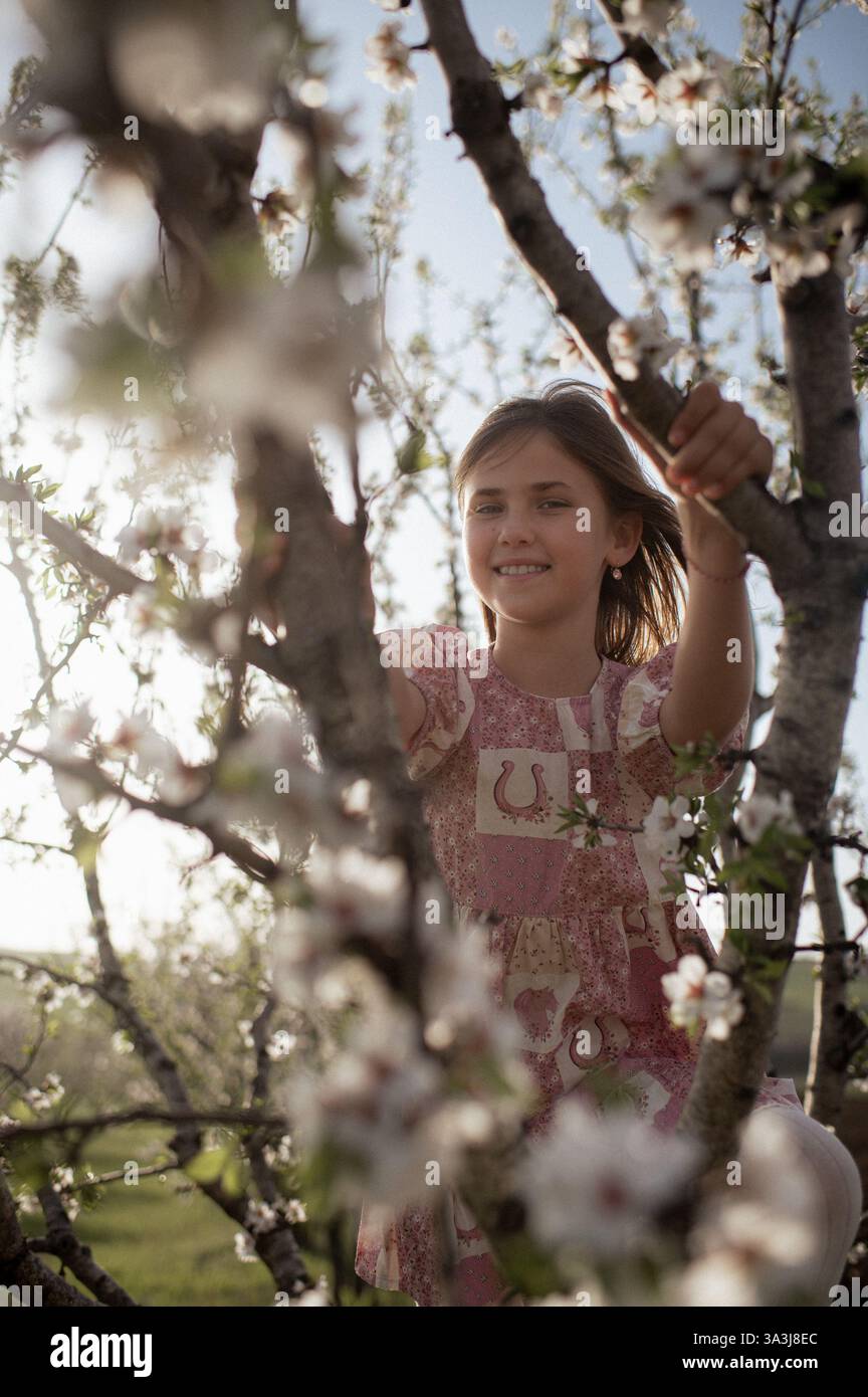 Ein fröhliches Mädchen spielt zwischen blühenden Mandelbäumen, ihr Lachen erfüllt die Frühlingsluft. Stockfoto
