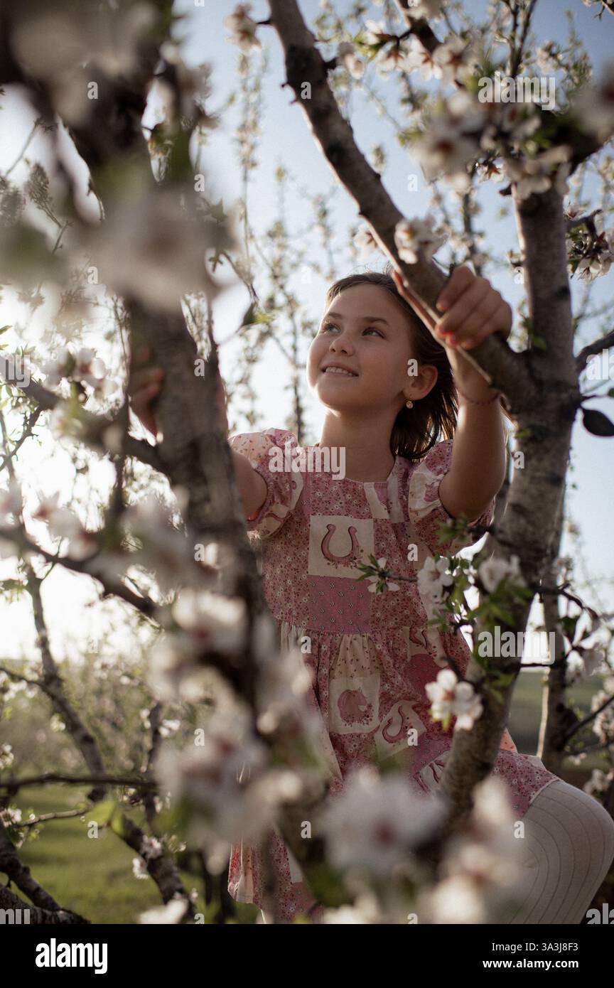 Ein fröhliches Mädchen spielt zwischen blühenden Mandelbäumen, ihr Lachen erfüllt die Frühlingsluft. Stockfoto